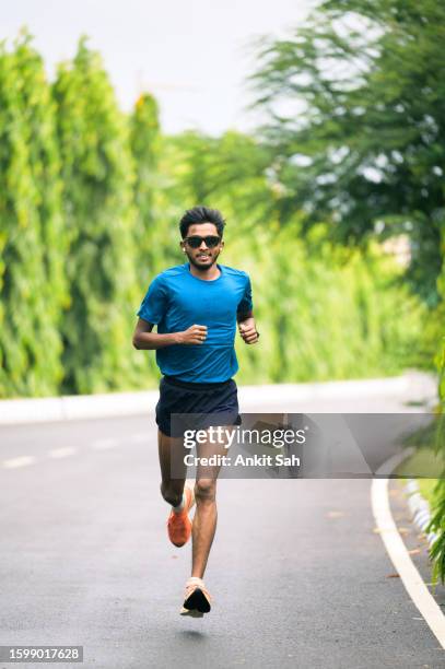 young athlete man running in park on concrete road at park. - sports india stock pictures, royalty-free photos & images
