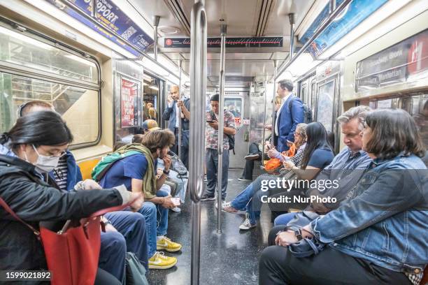 Daily life in New York's subway in Times Square with people sitting or standing inside the train carriage wagon while many are looking on their...