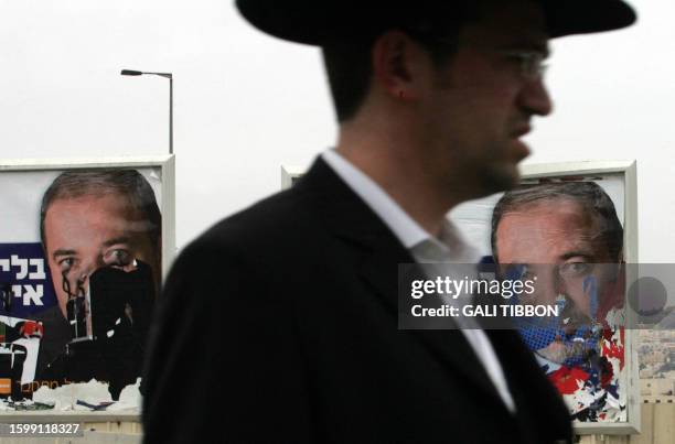 An Israeli walks past torn election campaign posters of Avigdor Lieberman, leader of the far-right Yisrael Beitenu party, in Jerusalem on February 8,...