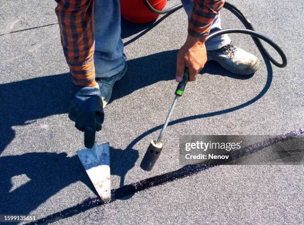 roofer preparing part of bitumen roofing felt roll for melting by gas heater torch flame - coating stockfoto's en -beelden