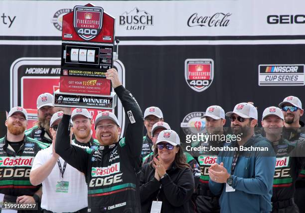 Chris Buescher, driver of the Castrol Edge Ford, lifts the FireKeepers Casino 400 trophy in victory lane after winning the NASCAR Cup Series...