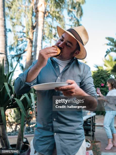 white man wearing hat bites into cheeseburger - 4k food stock pictures, royalty-free photos & images