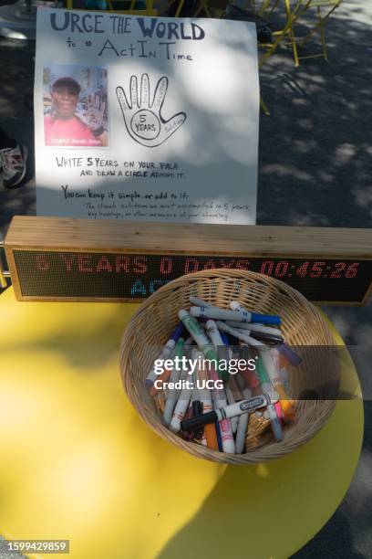 Poster, with instructions and a sample photograph of similar activities taking place globally, lays on a table with a portable Climate Clock and a...