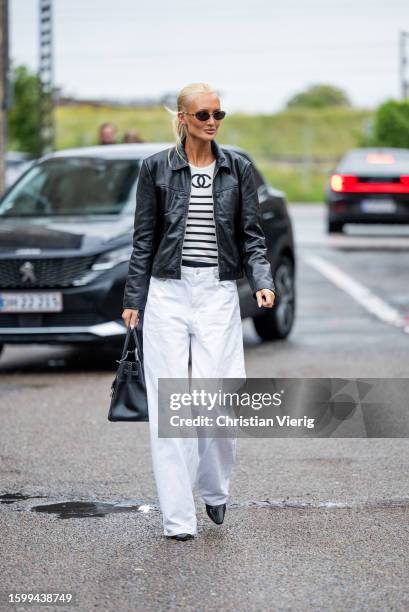 Guest wears white black striped shirt Chanel, black leather jacket, white pants, black bag outside 7 Days Active during the Copenhagen Fashion Week...