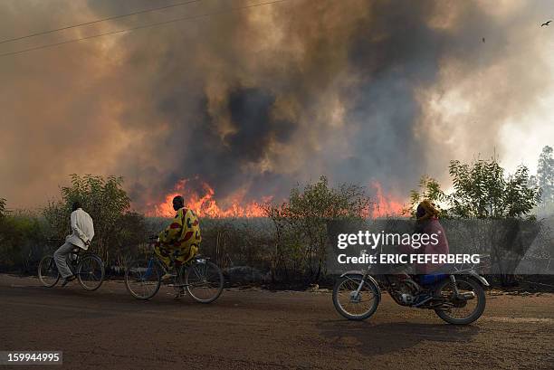 Cyclists pass a sugar cane field burning before the sugar cane harvest on January 23, 2013 near Niono, 370 kilometres north of the capital Bamako....