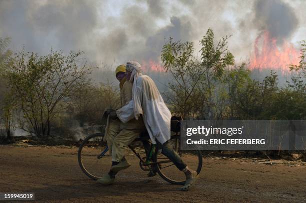 Cyclists pass a sugar cane field burning before the sugar cane harvest on January 23, 2013 near Niono, 370 kilometres north of Bamako. Malian...