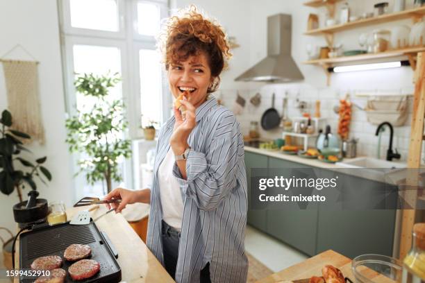 young beautiful woman making burgers in a domestic kitchen - woman cooking stock pictures, royalty-free photos & images