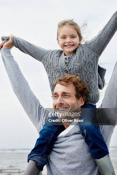 father carrying daughter on shoulders on the beach - auf den schultern stock-fotos und bilder