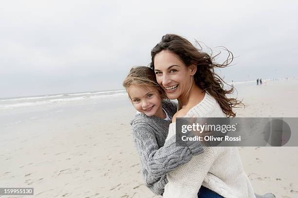 happy mother embracing daughter on the beach - tossing hair facing camera woman outdoors stock-fotos und bilder