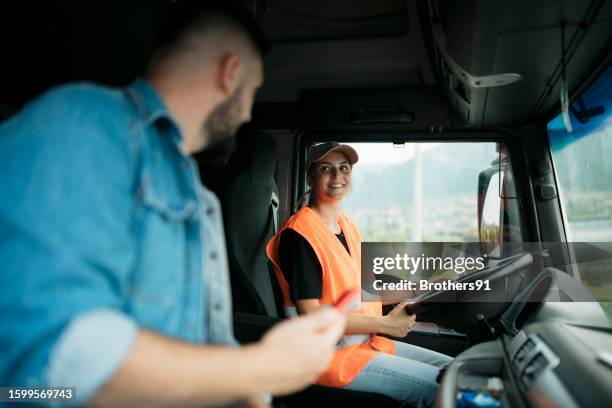 fahrerin, die einen lkw fährt und sich mit dem zusteller unterhält, der auf dem beifahrersitz sitzt - lkw kabine stock-fotos und bilder
