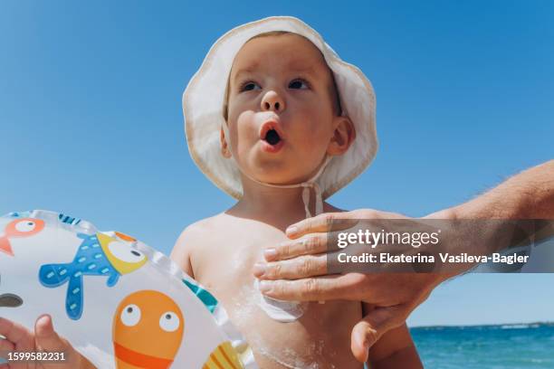 father rubbing suncream on son on beach - sun safety stock pictures, royalty-free photos & images