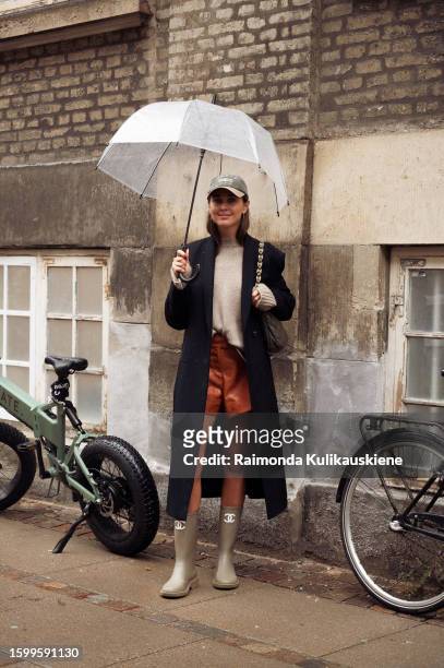Darja Barannik wearing brown leather shorts, light brown sweater, black coat, green cap, and haki Chanel rain boots outside A. Roege Hove during the...