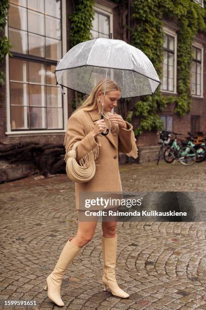 Guest wearing a beige coat with tassels, beige long shoes, transparent umbrella, and beige Bottega Veneta bag outside Herskind during the Copenhagen...