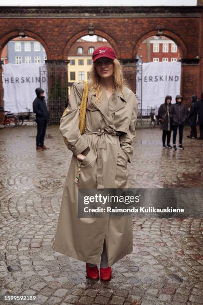 Guest wearing red shoes, a beige trench coat, and a red cap outside Herskind during the Copenhagen Fashion Week Spring/Summer 2024 on August 7, 2023...