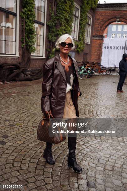 Grece Ghanem wearing a beige skirt, long black boots, silk white and black top, brown leather jacket, black sunglasses, and Louis Vuitton bag outside...