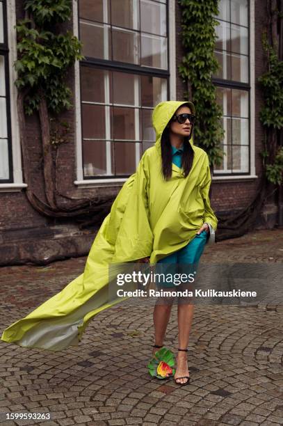Guest wearing a blue dress, lime green coat, Loeve flower shoes, and black sunglasses outside Herskind during the Copenhagen Fashion Week...
