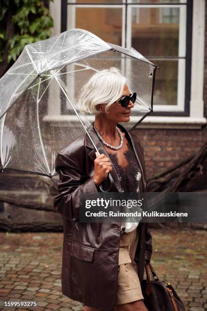 Grece Ghanem wearing a beige skirt, long black boots, silk white and black top, brown leather jacket, black sunglasses, and Louis Vuitton bag outside...