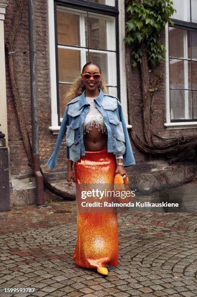 Petra Henriette Rufi wearing an orange maxi skirt, white cropped top with hanging rain stones, blue denim jacket, orange shoes and orange fur bag...