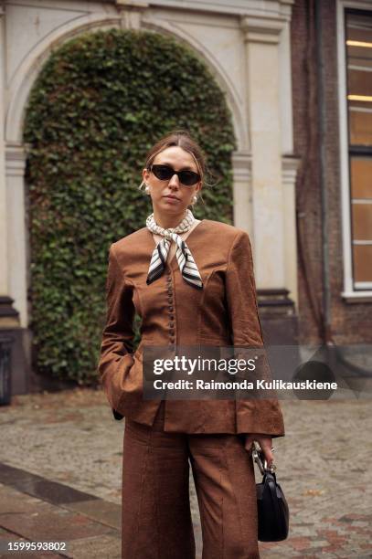 Guest wearing a brown jacket, brown pants, and silk neck scarf outside Herskind during the Copenhagen Fashion Week Spring/Summer 2024 on August 7,...