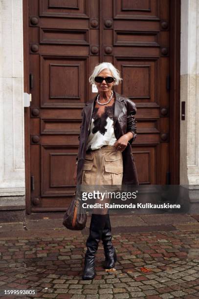 Grece Ghanem wearing a beige skirt, long black boots, silk white and black top, brown leather jacket, black sunglasses, and Louis Vuitton bag outside...