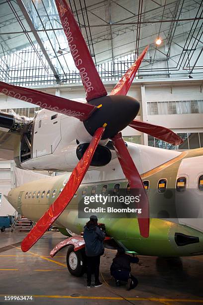 Employees stand beneath the propellers of a Pratt & Whitney engine as they check the fuselage of an ATR-72 turboprop aircraft, manufactured by Avions...