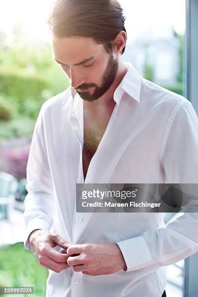 a young bearded man unbuttoning his shirt - buttoning shirt stockfoto's en -beelden