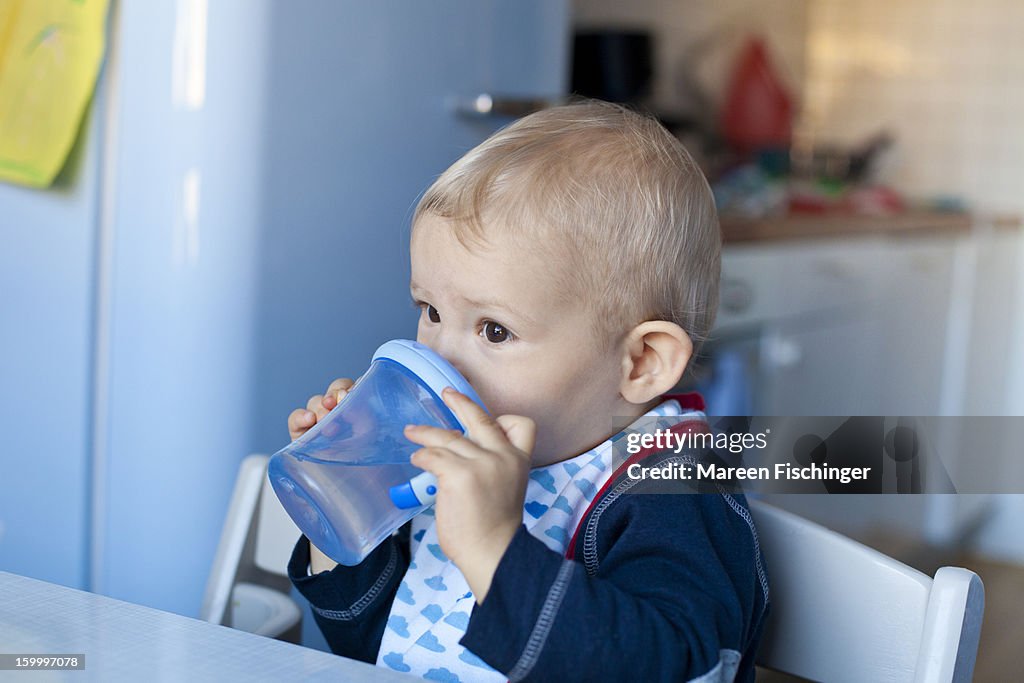 Baby drinking water out of a baby cup in a kitchen