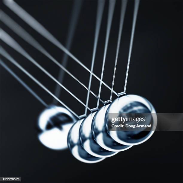 a chrome ball on a newtons cradle swinging to hit - newtons cradle stockfoto's en -beelden