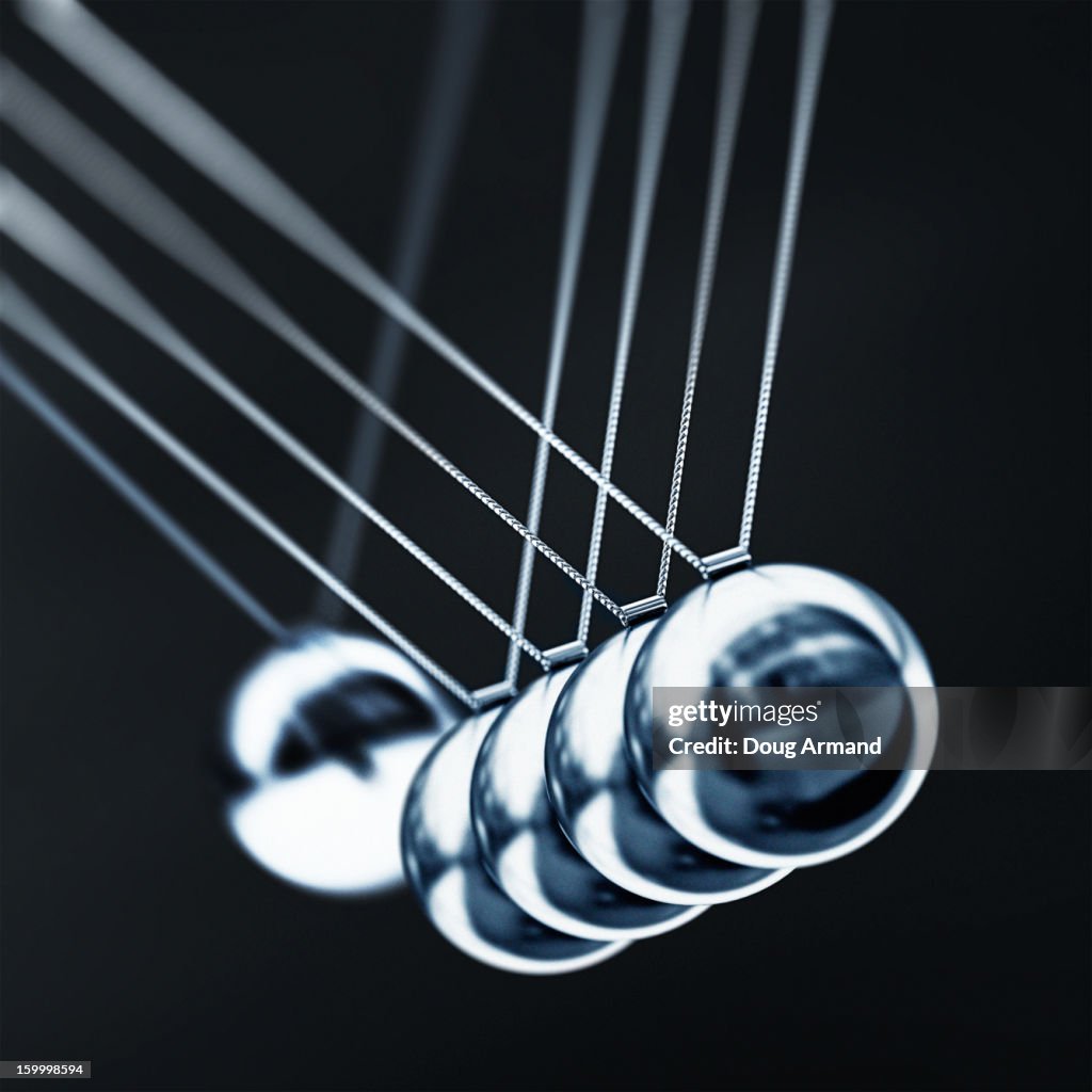 A chrome ball on a newtons cradle swinging to hit