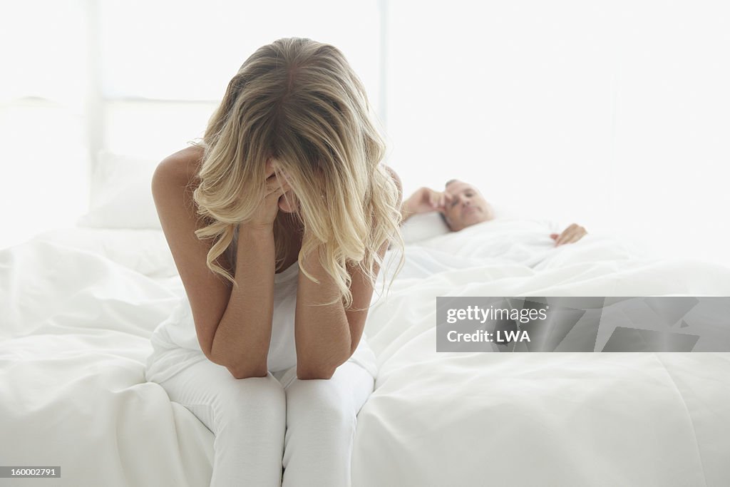 Woman holding head in hands sitting at foot of bed