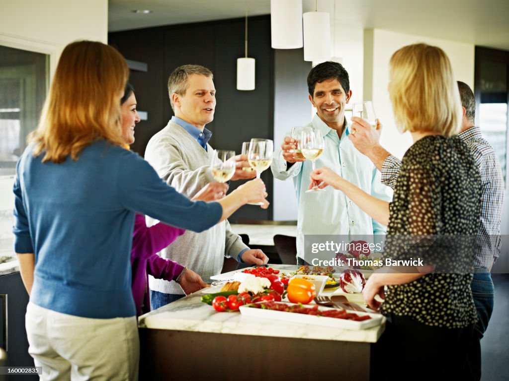 Couples in home kitchen toasting wine glasses