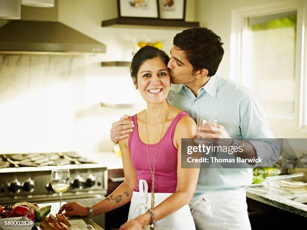 husband kissing wife on cheek in home kitchen - indian wife stock pictures, royalty-free photos & images