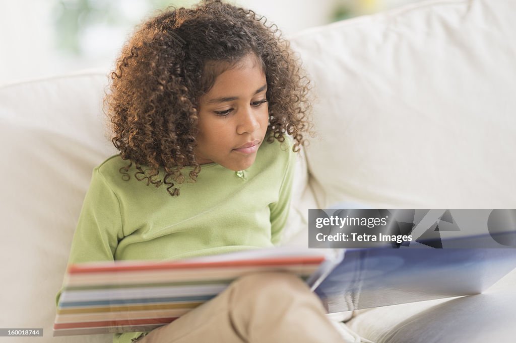 Girl (6-7) reading book on sofa