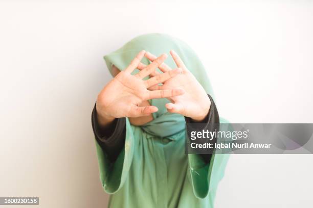 asiatisches muslimisches junges mädchen öffnet die handfläche in die kamera und bedeckt sein gesicht. stopp-geste - islamfeindlichkeit stock-fotos und bilder