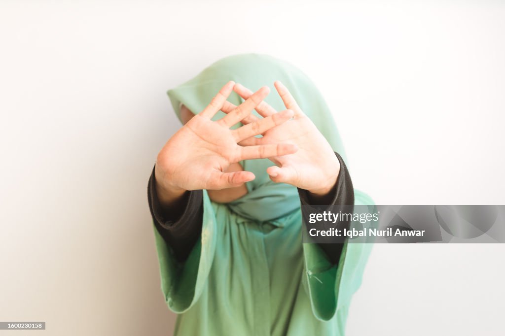 Jovem muçulmana asiática abre a palma da mão para a câmera, cobrindo seu rosto. Gesto de parar