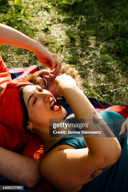 young couple lying on a field and eating cherrys - friends picnic stock pictures, royalty-free photos & images