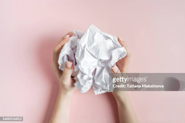 crumpled white paper in female hands on a pink background top view. concept of creativity and failed idea. - papierkugel stock-fotos und bilder