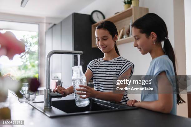seitenansicht von zwei jungen mädchen in der küche, die ein glas mit leitungswasser füllen - wasserglas stock-fotos und bilder