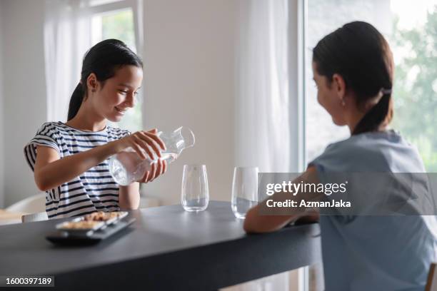 a young multiracial girl is smiling and serving some water into a glass - girl filling water glass stock pictures, royalty-free photos & images