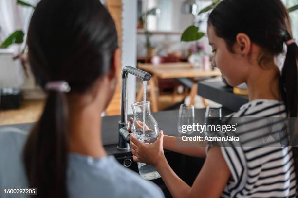 back of two young sisters filling a glass jar with some tap water at the kitchen - girl filling water glass stock pictures, royalty-free photos & images