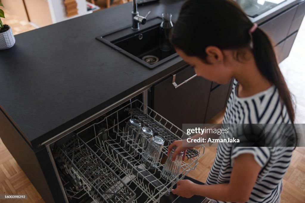Aerial View Of A Young Multiracial Young Girl Putting A Glass Inside The Tray Of A Dishwasher