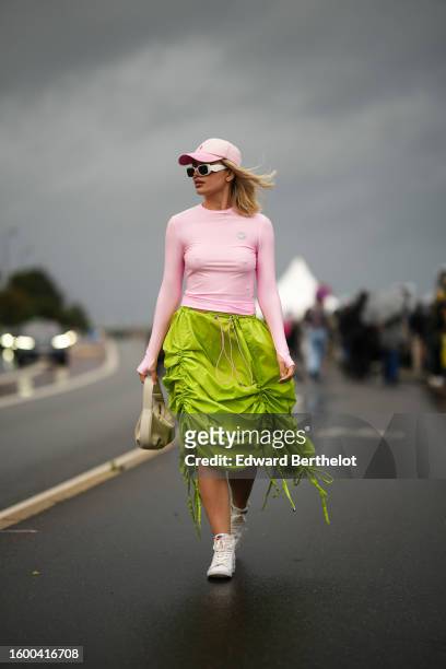 Guest wears a pale pink denim with purple B embroidered pattern cap, white matte sunglasses from Prada, a pale pink long sleeves nylon t-shirt, a...