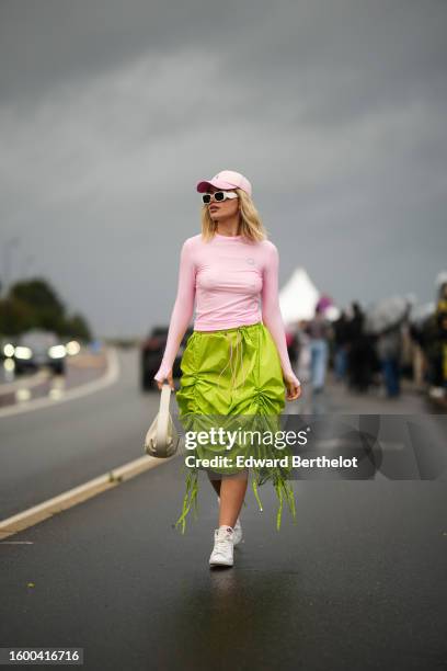 Guest wears a pale pink denim with purple B embroidered pattern cap, white matte sunglasses from Prada, a pale pink long sleeves nylon t-shirt, a...