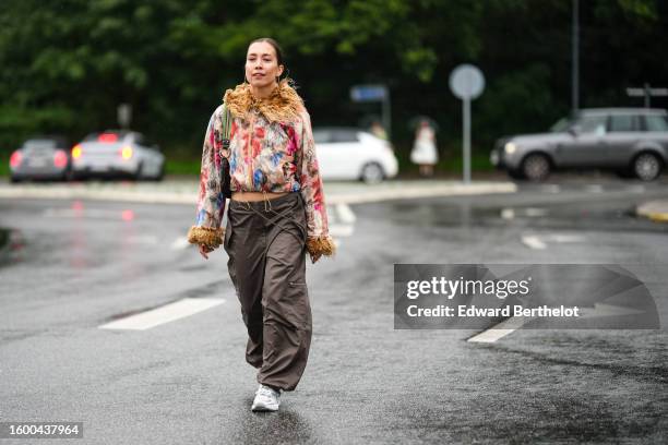 Guest wears gold earrings, a beige / pink / blue / green print pattern fur zipper bomber coat, a black shiny leather with green strap shoulder bag,...