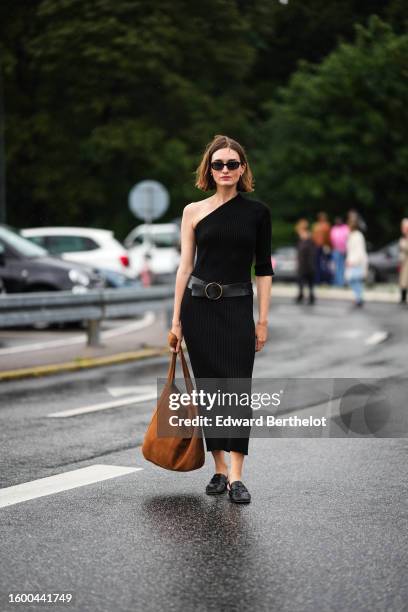 Guest wears black sunglasses, a black asymmetric shoulder / one long sleeve / long tube dress, a black shiny leather large belt, a camel suede large...