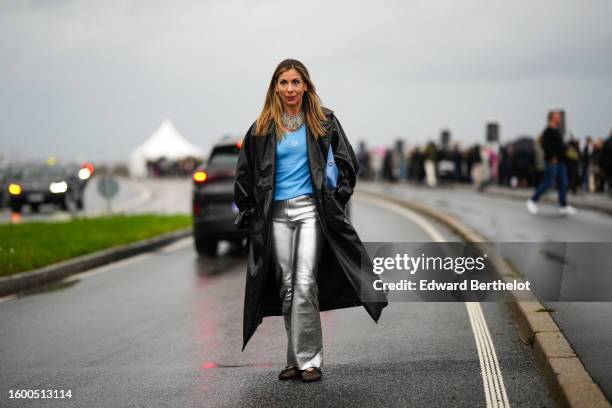 Guest wears a silver fringed long and large necklace, a blue ribbed tank-top from Loewe, a black shiny leather long coat, silver shiny leather flared...