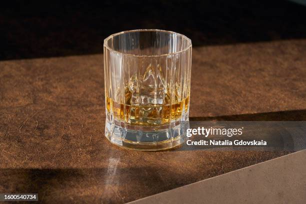 glass of whisky with ice on dark table. special kind of drink that grown-ups enjoy. made from grains like barley, rich and unique flavor. ice cubes floating in glass for nice and cool, ice-cold drink on hot day. - cognac glass stock-fotos und bilder