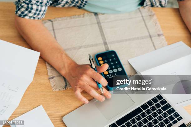 man using calculator, analyzing financial data. focused on work and working on budget or expense report. man sitting at table in well-lit office. - financial literacy stock pictures, royalty-free photos & images
