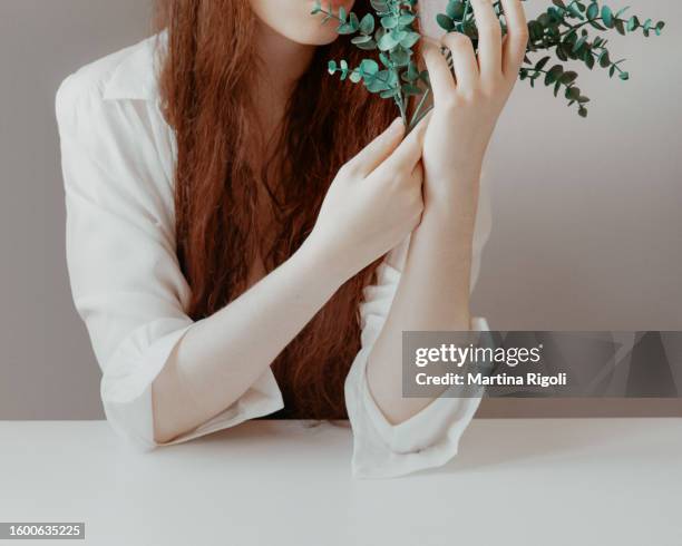 long-haired redhead young woman with pale skin holding eucalyptus leaves - silver blouse stock pictures, royalty-free photos & images