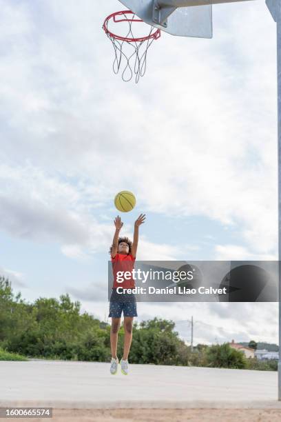 boy jumping while playing on a basketball court - jump shot basketball stock pictures, royalty-free photos & images